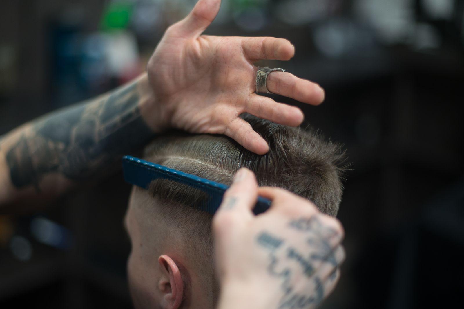 Barbeiro tatuado fazendo um corte degradê com pente e máquina