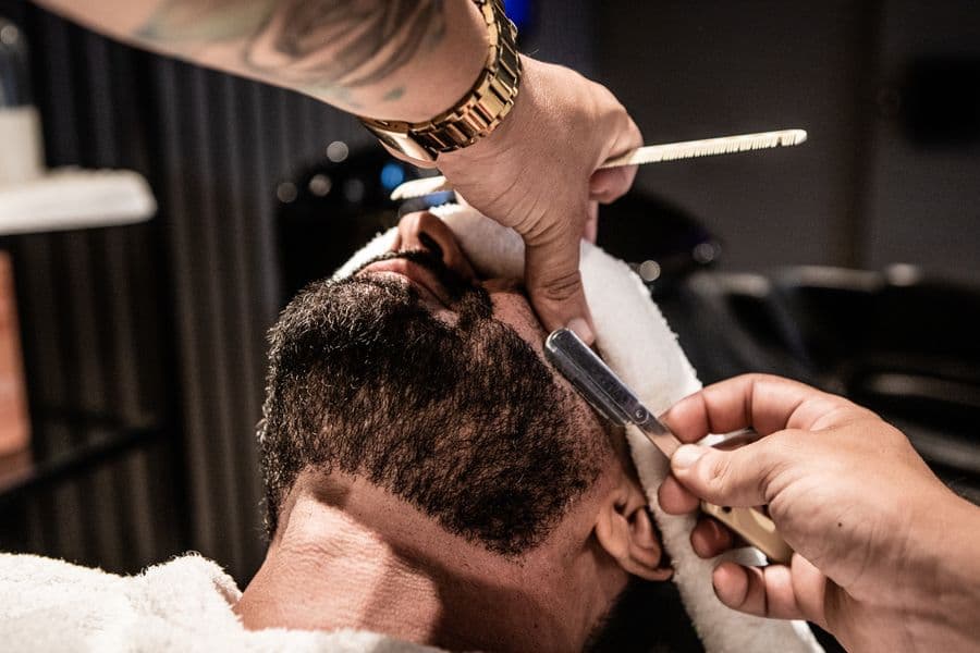Barbeiro acertando a barba de um cliente com navalha