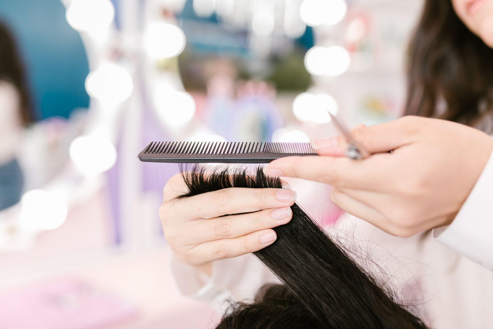 Mãos de cabeleireira penteando e cortando o cabelo de uma cliente no salão